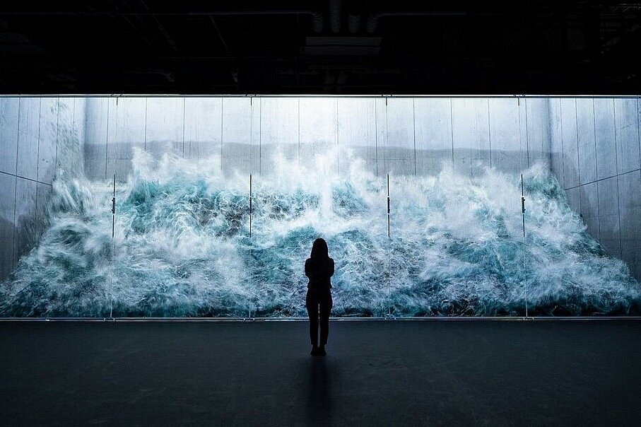 A visitor is silhouetted against a towering digital wave installation